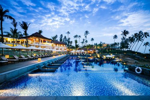 - une piscine avec des chaises longues et des palmiers la nuit dans l'établissement Anantara Peace Haven Tangalle Resort, à Tangalle