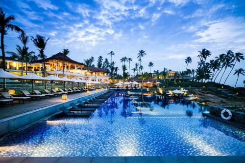 a resort pool with chairs and palm trees at night at Anantara Peace Haven Tangalle Resort in Tangalle