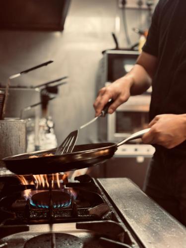 a person cooking food in a pan on a stove at The White Horse Inn in Washford
