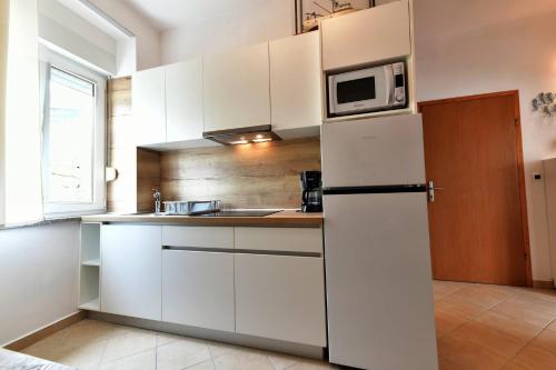 a white kitchen with a refrigerator and a microwave at Apartments Barbalic Beach in Baška