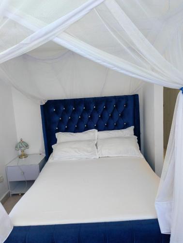 a bed with a blue headboard and a white canopy at Modern Couzy Suites in Malindi