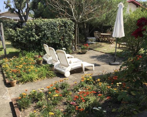 two white chairs and an umbrella in a garden with flowers at maison proche du centre et de la plage in Soulac-sur-Mer
