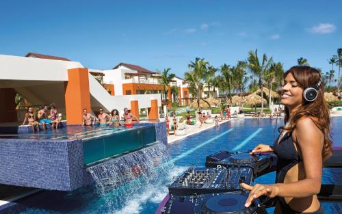Una mujer con auriculares de pie junto a una piscina en un complejo turístico. en Breathless Punta Cana Resort & Spa - Adults Only - All Inclusive, en Punta Cana