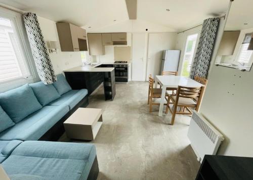 un salon avec un canapé bleu et une cuisine dans l'établissement Mobil home de standing aux portes des Cévennes sur un terrain ombragé et arboré, à Anduze