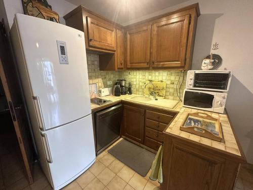 La cuisine est équipée d'un réfrigérateur blanc et de placards en bois. dans l'établissement Appartement à proximité de la plage, à Saintes-Maries-de-la-Mer