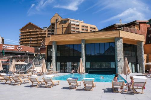 a pool with chairs and umbrellas in front of a building at Belambra Clubs Les 2 Alpes Les Crêtes in Les Deux Alpes