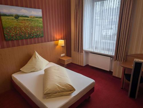 a hotel room with a bed with white sheets and pillows at Stadthotel Augsburg in Augsburg