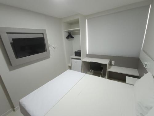Habitación blanca con cama, escritorio y TV. en Trip Hotel Ubá - perto da Faculdade OZANAM COELHO e Eventos HORTO FLORESTAL, en Ubá