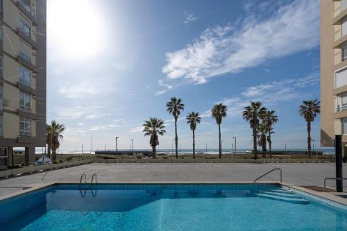 a swimming pool with palm trees in front of a building at Horizonte Azul , Frente mar & Piscina in Costa da Caparica