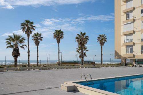 a swimming pool with palm trees and a building at Horizonte Azul , Frente mar & Piscina in Costa da Caparica