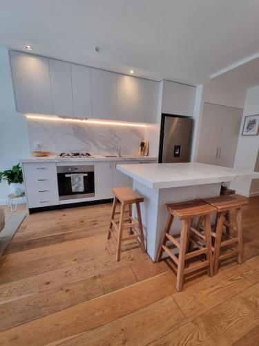a kitchen with a white counter and wooden stools at Regent Retreat Top floor apartment in Melbourne