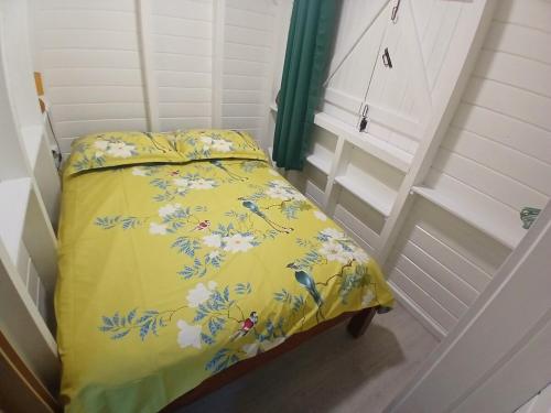 a small bed with a yellow blanket with flowers on it at Bungalow Lolo Moringa in Bouillante