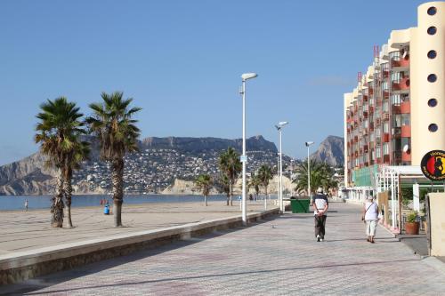 a beach with palm trees and people walking down a sidewalk at Amatista 12 D - Private in Calpe