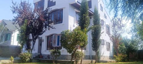a white house with trees in front of it at Magnolia Homestay in Srinagar
