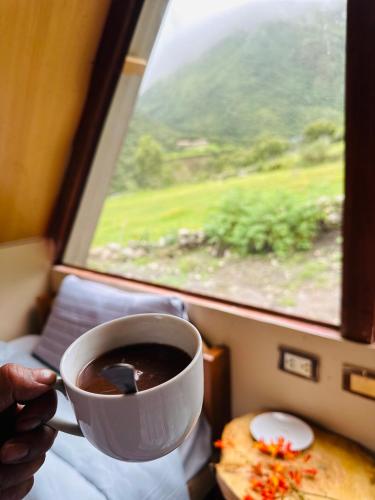 una persona sosteniendo una taza de café frente a una ventana en Salkantay Glamp, en Colcapampa