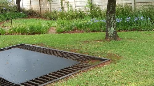a metal grate in the grass next to a tree at African Silhouette Guesthouse in Benoni