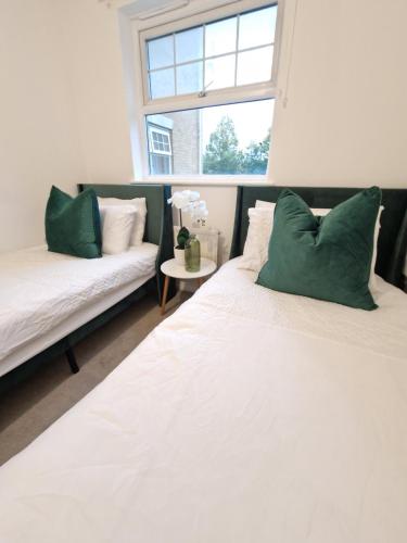 two beds with green pillows in a room with a window at Apartment Near Wembley Stadium Heathrow London Barnet Luton Airport Hendon Middlesex University - FREE Parking & WiFi - Work Contractors & Tourists Welcome in Edgware