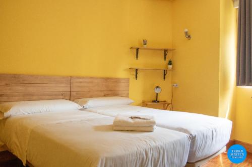 two beds in a room with yellow walls at Txoko Maitea Pentsioa in Urnieta