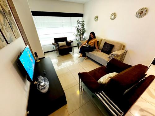 a woman sitting on a couch in a living room at Ecuabook Wyndham Garden Torre Sol 907 in Guayaquil