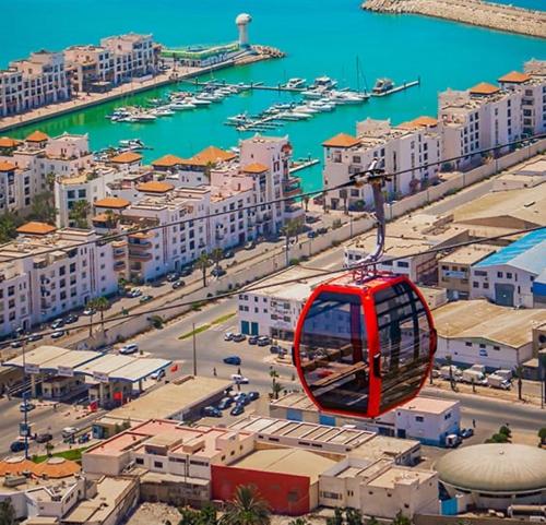 a red cable car flying over a city at Appartement vue panoramique sur mer Avec Climatisation! à 5 minutes à pied de la Plage ! à environ 6 minutes en voiture du Centre d'Agadir et à 10 minutes en voiture de Taghazout ! in Agadir