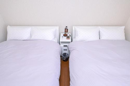two beds with white sheets and a night stand between them at Bhome Hikone Jizo in Hikone
