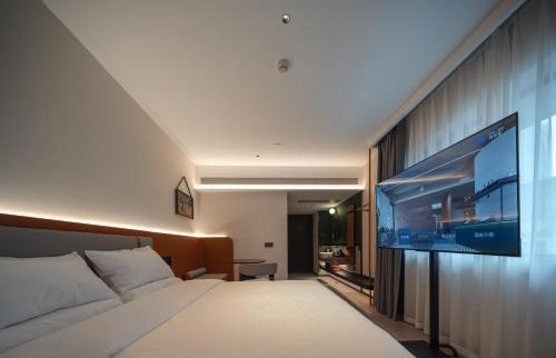 a hotel room with a bed and a flat screen tv at 欢桔酒店 郑州二七广场丹尼斯大卫城店 in Zhengzhou