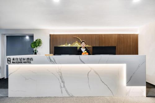 a woman standing behind a reception desk in a lobby at NICESOE Hotel - Chengdu Jianshe Road Electronic Science University in Chengdu