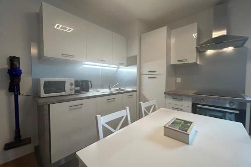 une cuisine avec des armoires blanches et une table avec un micro-ondes dans l'établissement Spacious appt with balcony in the 13th, à Paris