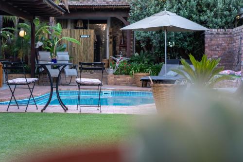 a patio with an umbrella and chairs and a pool at Earthbound Guest House in Oudtshoorn