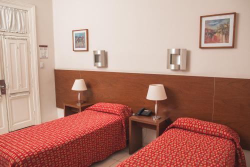 two beds in a hotel room with red sheets at Gran Hotel Victoria Cordoba Argentina in Cordoba
