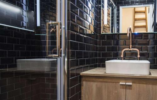 une salle de bain carrelée noire avec un lavabo et un miroir dans l'établissement Alpohi, à Paris