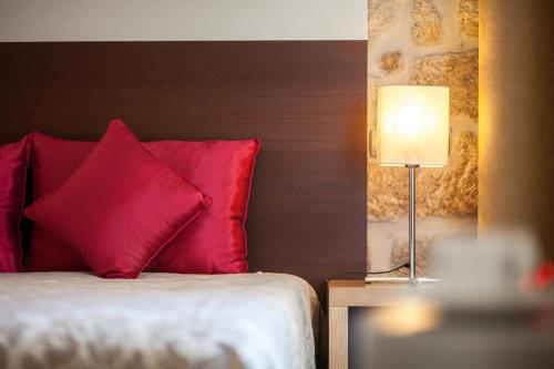 a bed with a red pillow and a table with a lamp at Casas Novas Countryside Hotel Spa & Events in Chaves