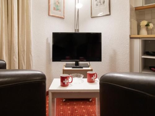 uma sala de estar com uma TV e duas canecas sobre uma mesa em Apartment Chalet Abendrot apARTments-6 by Interhome em Grindelwald