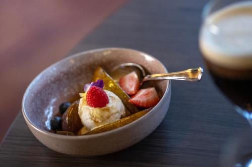a bowl of fruit with a spoon and a glass of wine at Hotel Korpilampi in Espoo