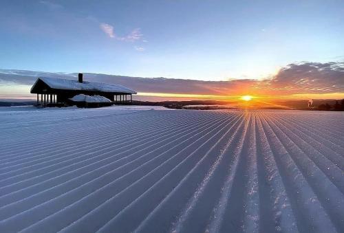 a snow covered field with a barn in the sunset at Nice ski in ski out cabin in Bollnäs