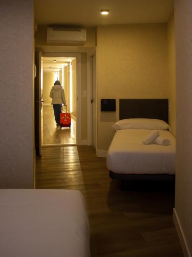 a woman with a red suitcase walking through a room with two beds at Pension Roomtegi in Barakaldo