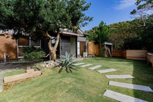 un patio trasero con un árbol y un camino de piedra en サウナ付き一棟貸し宿 築ける宿 - sudaku, en Iwada