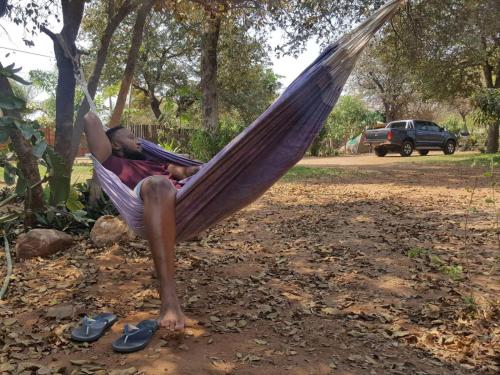 a man is sleeping in a hammock at Nxabii Cottages in Kasane
