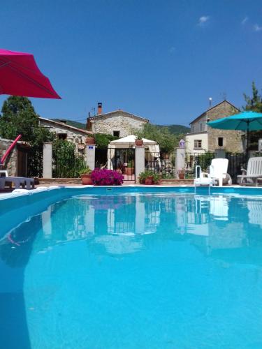 une grande piscine bleue avec un parasol rouge dans l'établissement Le Mas Joyeux - L'Olivier - Gîte En Cévennes, à Saint-Florent-sur-Auzonnet