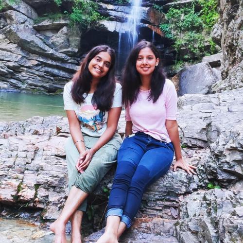 two women sitting on a rock in front of a waterfall at Moonlight Camp Dhanachuli Mukteshwar in Nainital