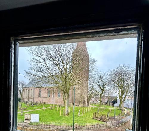 a window view of a church with a large tower at Bovenop 19 in Hippolytushoef