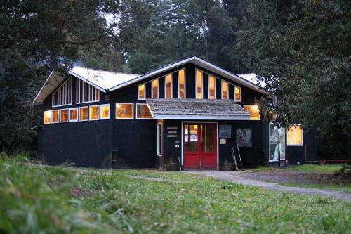 a black house with a red door in a yard at Centro Turístico Anticura Parque Nacional Puyehue in Anticura