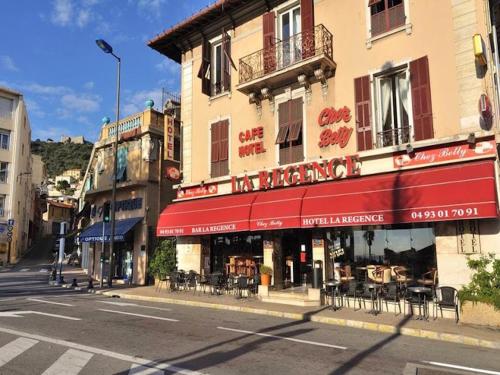 ein Gebäude mit einer roten Markise auf einer Stadtstraße in der Unterkunft Hotel La Regence in Villefranche-sur-Mer