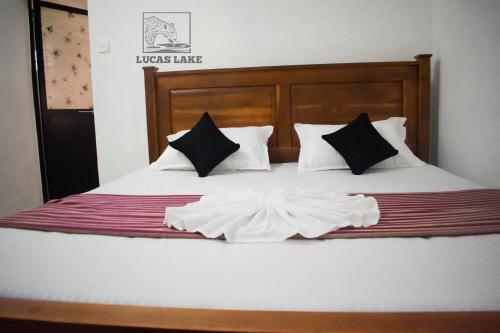 a bedroom with a bed with white sheets and black pillows at Yala Lucas Lake Hotel in Tissamaharama