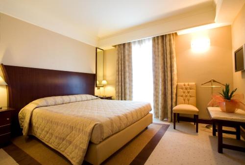 a bedroom with a bed and a chair and a window at Grand Hotel Olimpo in Alberobello