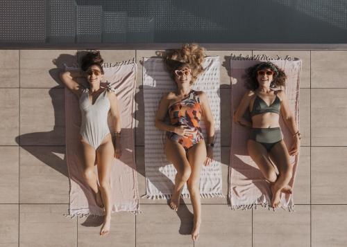 three women in bathing suits sitting on towels on a beach at GOING TRIPLE A apartments WEST in Going