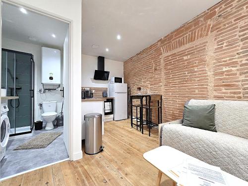 un salon avec un canapé et un mur de briques dans l'établissement Le Briand - Studio pour 2 personnes - Climatisation - Fibre internet - 5 min à pied de la gare et du centre-ville - Places de stationnements gratuites sur toute l'avenue, à Montauban
