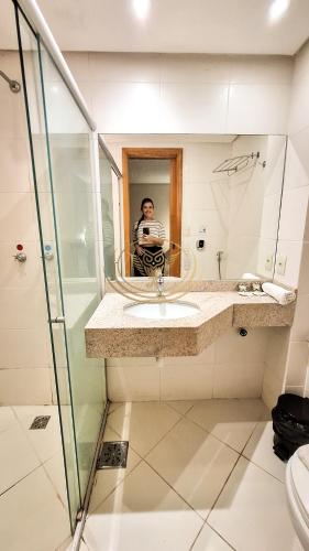 a man taking a picture in a bathroom mirror at Coruja Imob - Flat Crystal Place in Goiânia
