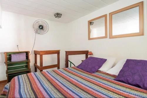 a bedroom with a bed with purple pillows and a fan at Buzios Casa #6 in Búzios