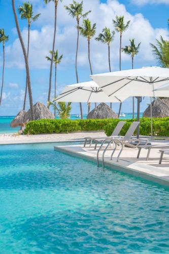 a pool with chairs and umbrellas and the ocean at Xeliter Playa Coral, Bavaro in Punta Cana